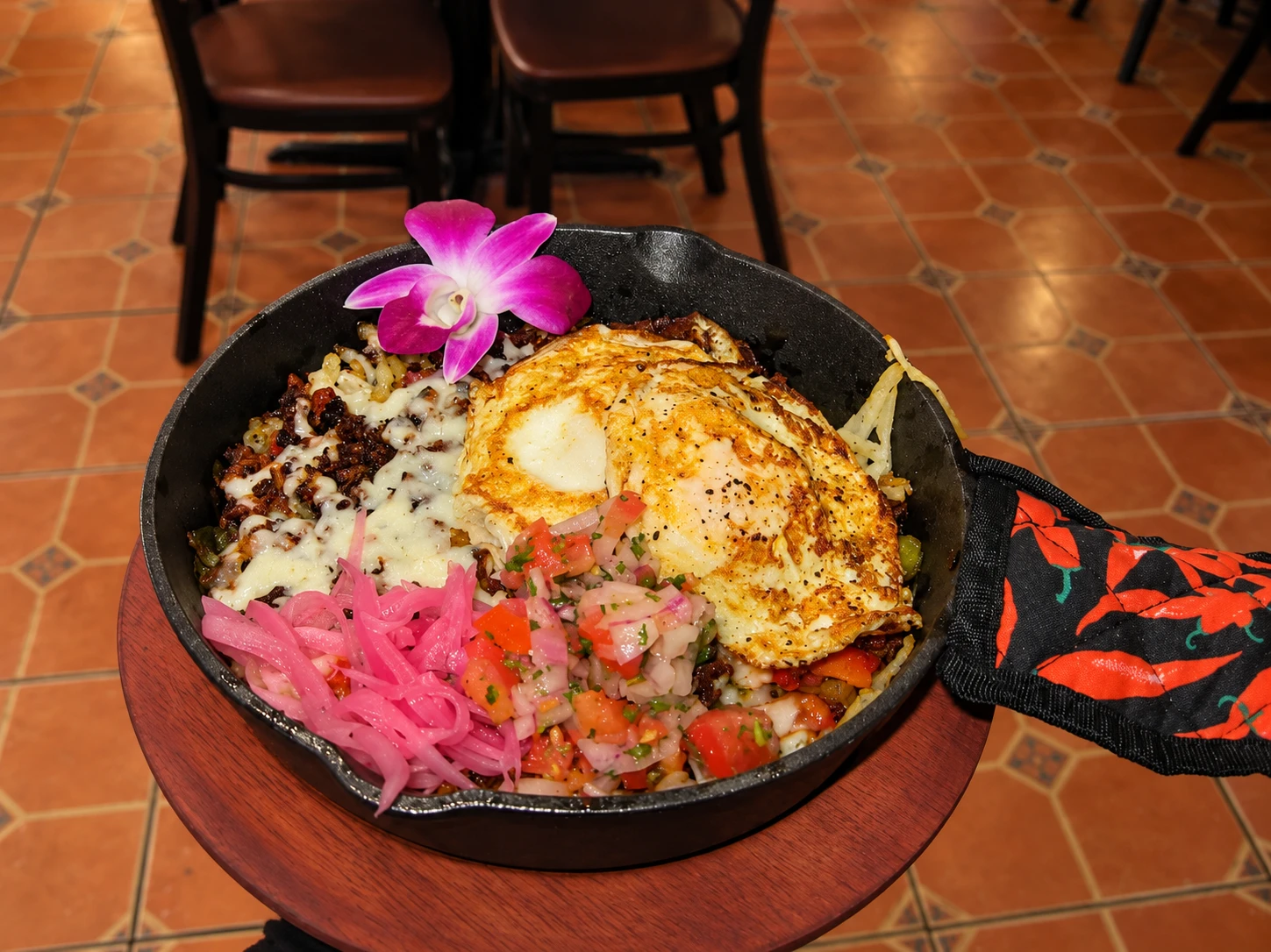 Breakfast skillet topped with fried eggs, melted cheese, pico de gallo and pickled onions