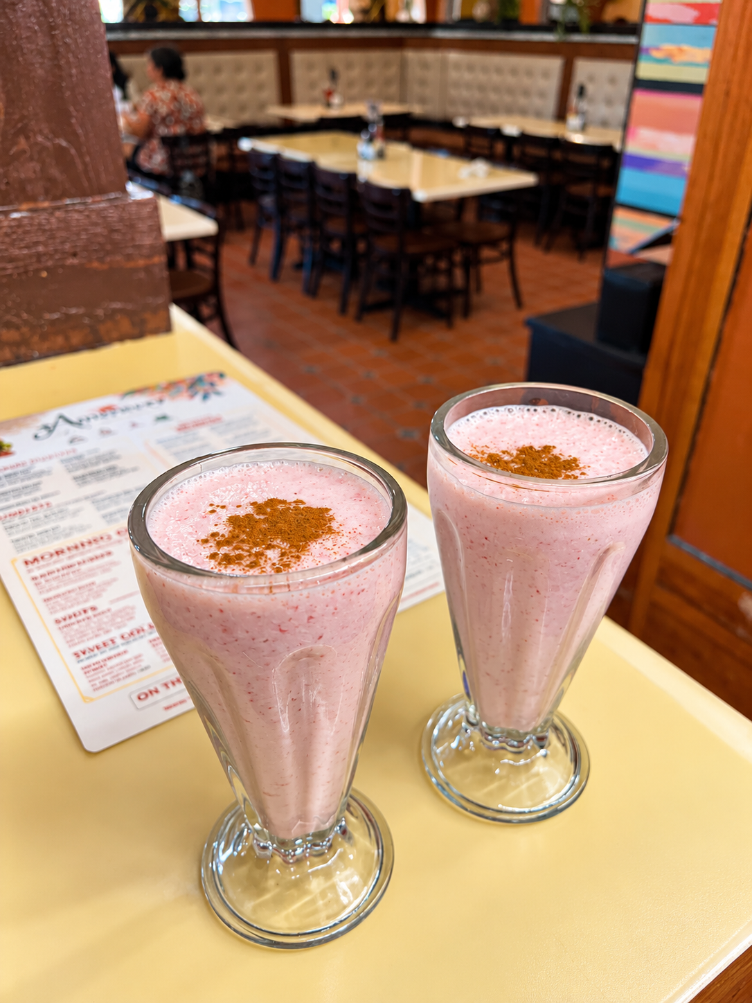 Two strawberry licuadas dusted with cinnamon beside the Amanecer menu