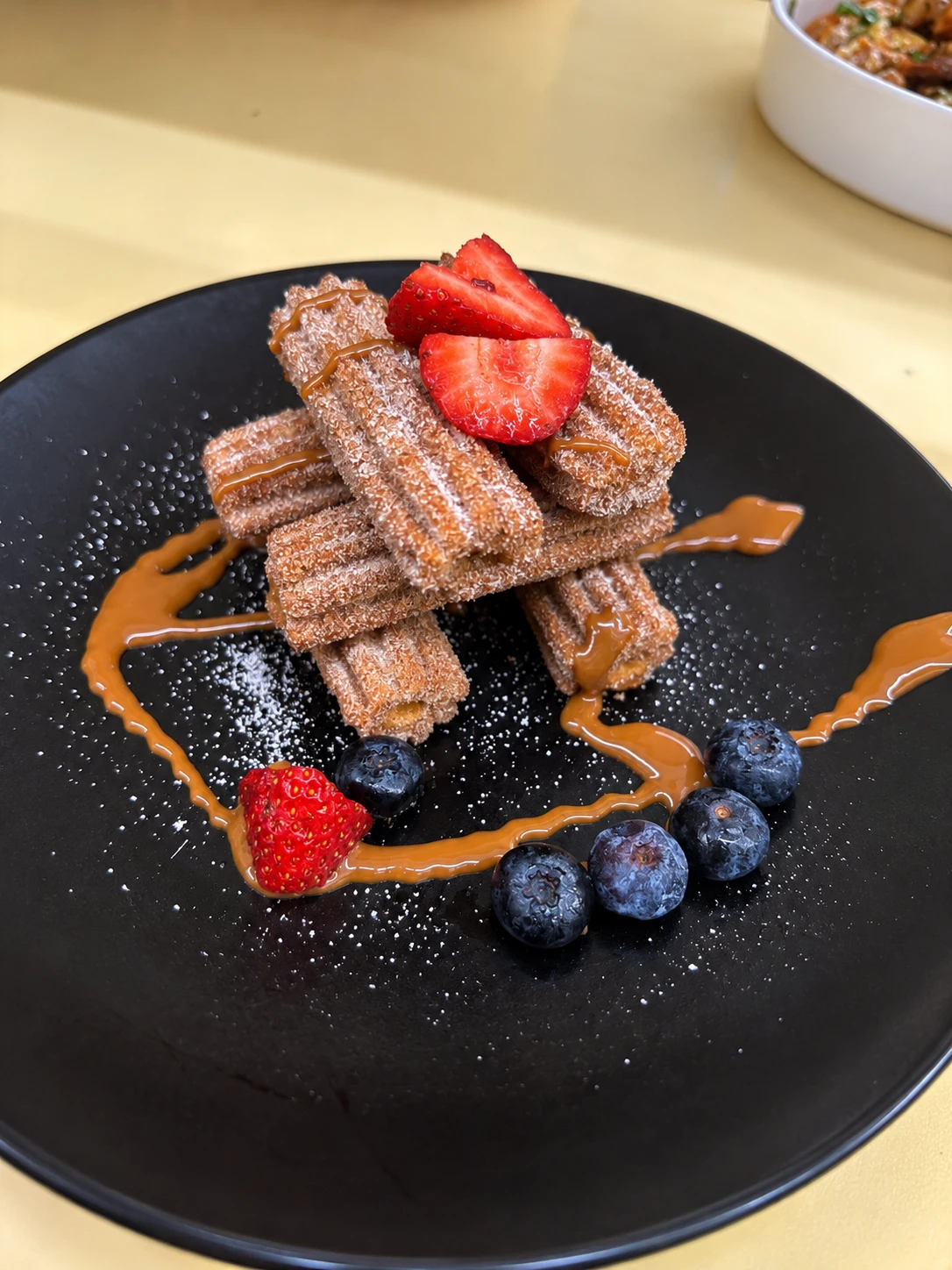 Sugar-coated churros with strawberries, blueberries and caramel drizzle