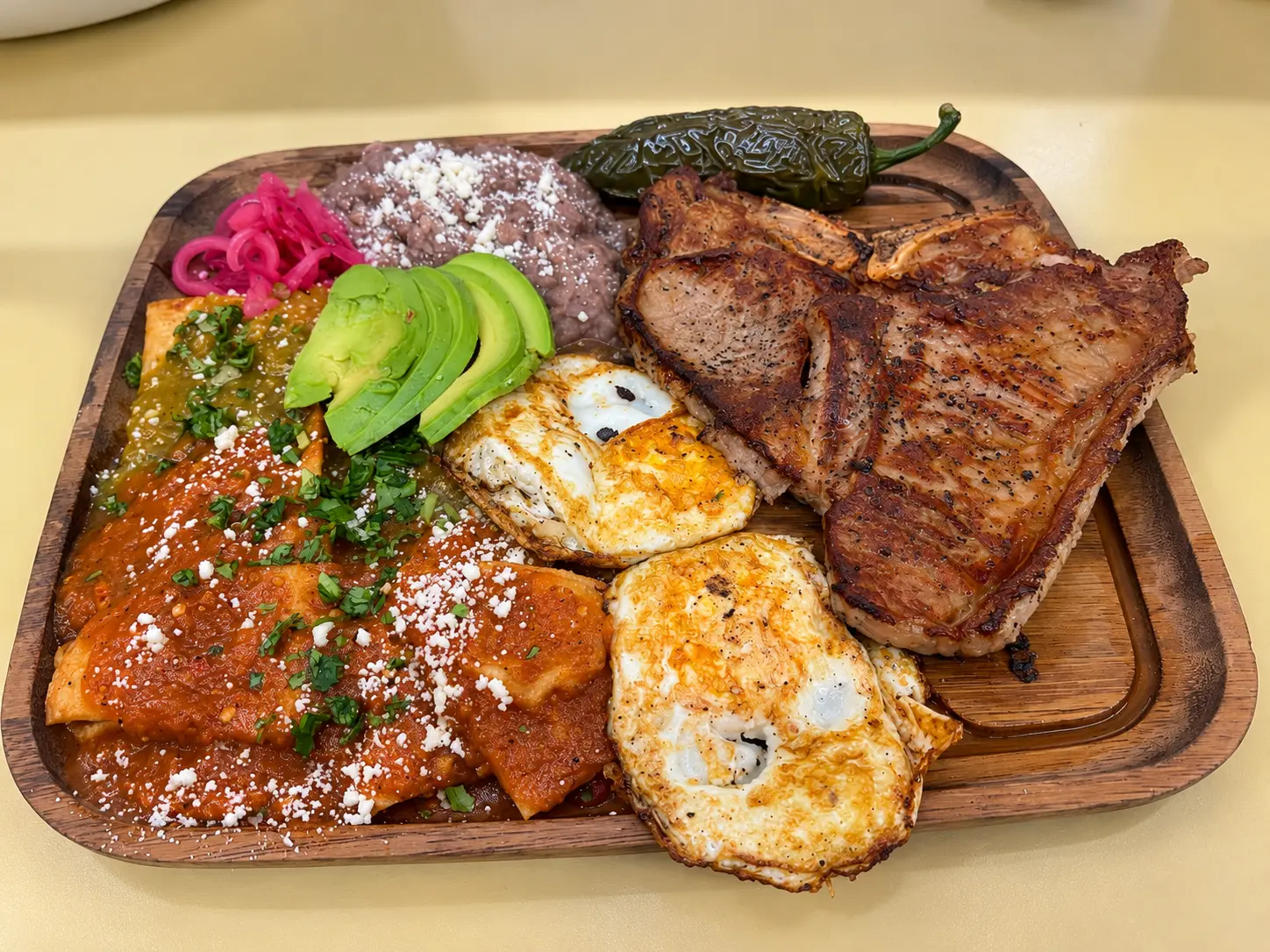 Breakfast platter with grilled pork chops, eggs, chilaquiles, beans and avocado
